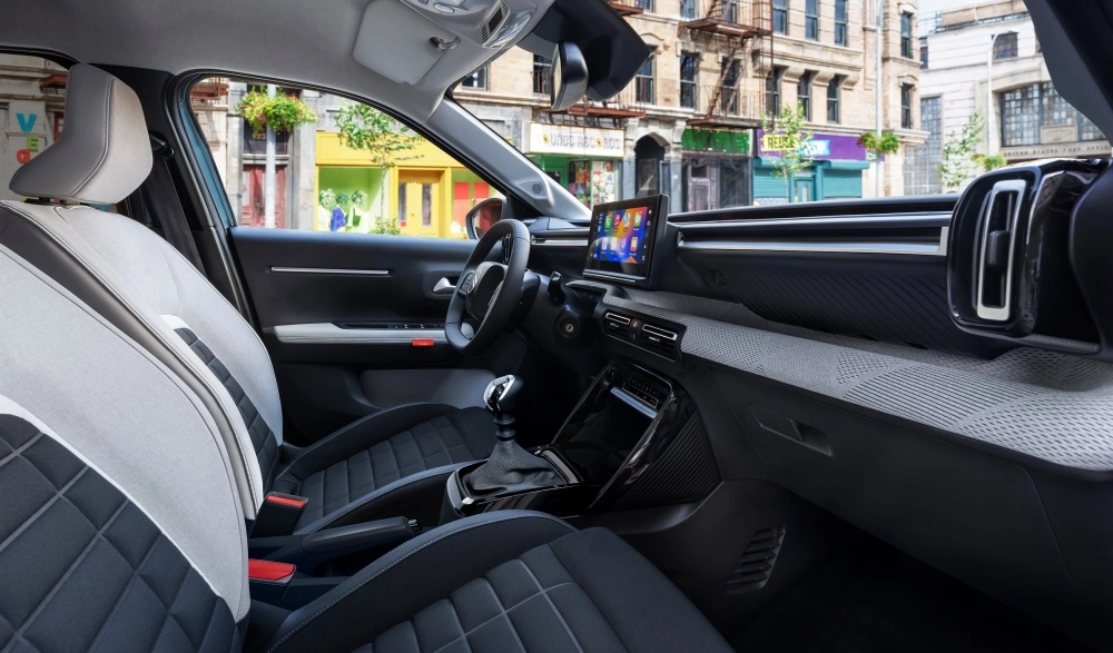 Citroen e-C3 elektrikli SUV modelinin ferah iç mekan tasarımı, gri ve siyah kumaş döşemeli konforlu koltukları, direksiyon simidi, merkezi dokunmatik ekranı ve modern kokpit detayları ile şehir içinde şık bir sürüş deneyimi sunuyor.