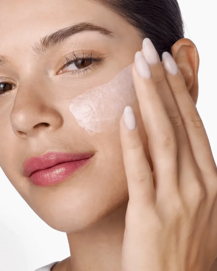 Cildine nemlendirici bir gece maskesi uygulayan, pürüzsüz tenli ve dudaklarında pembe ruj olan genç bir kadın, Clinique Moisture Surge gibi yoğun nemlendirme sağlayan ürünlerin cilt üzerindeki faydasını görselleştiriyor.