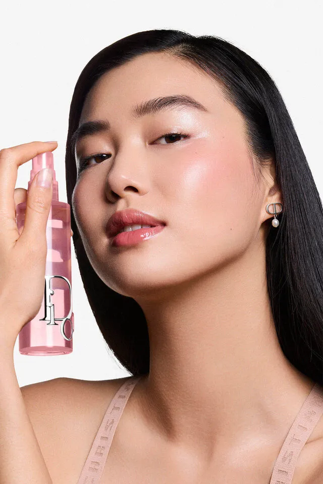 Parlak pembe dudaklara, ışıltılı pembe yanaklara ve pürüzsüz tene sahip Asyalı bir model, sağ elinde pembe renkli Dior Backstage Airflash Mist sprey şişesini yüzüne doğru tutarak ürünün tazeleyici etkisini vurguluyor.