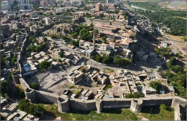 Diyarbakır Kalesi'nin İçkale bölgesi ve geniş surları, havadan çekilen bu karede görkemli bir şekilde yükselirken, surların içindeki tarihi yapılar ve dışarıda Dicle Nehri'ne uzanan yemyeşil Hevsel Bahçeleri, Türkiye'deki bu özel UNESCO Dünya Mirası alanının kadim kültürel peyzajını ve doğayla iç içe geçmiş uyumunu net bir şekilde gözler önüne seriyor.