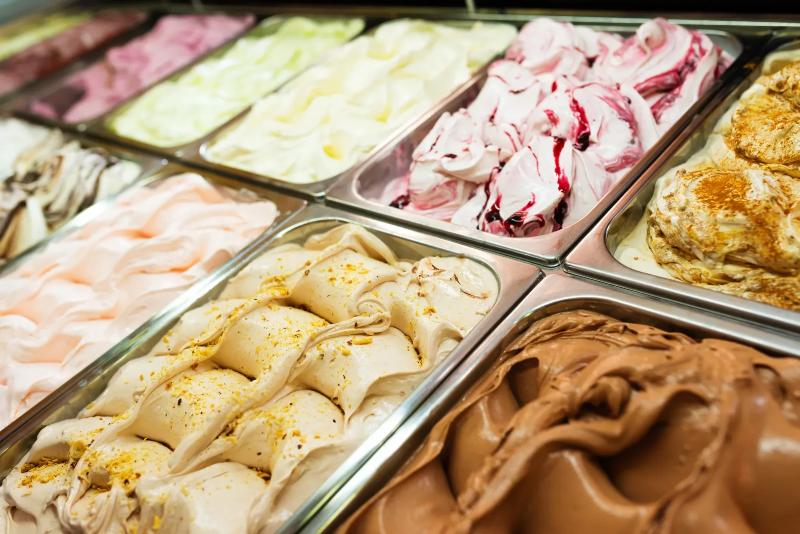 Metal kaplarda sıralanmış, farklı renk ve dokularda, bazıları meyve soslu, bazısı fındık veya baharat serpilmiş çikolatalı ve karamelli gibi birçok dondurma ve gelato çeşidi, bu iki tatlı arasındaki zengin çeşitliliği gözler önüne seriyor.