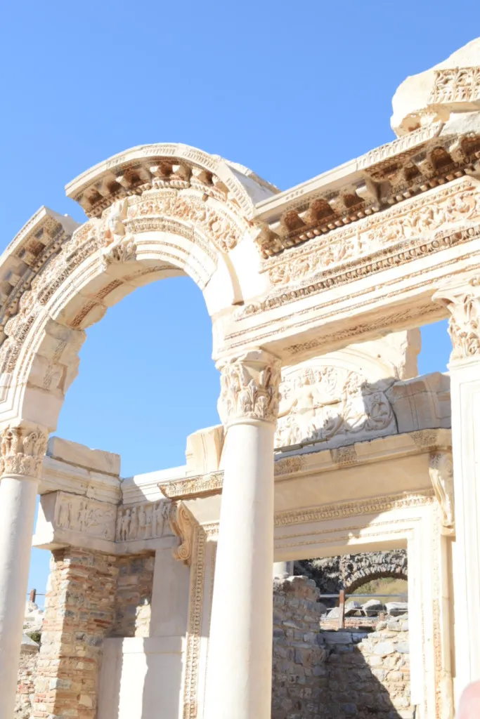 Efes Antik Kenti'ndeki Hadrian Tapınağı'nın detaylı kabartmalarla süslü mermer kemerli girişi, güneşli açık mavi bir gökyüzünün altında antik bir dönemin ihtişamını gözler önüne seriyor ve Türkiye'deki kültürel UNESCO Dünya Mirası rotaları arasında ziyaretçilerini bekliyor.