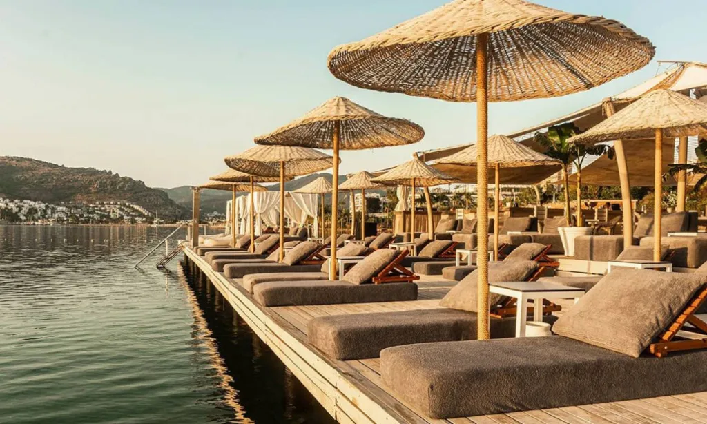 Escape Beach & Lounge Gündoğan’da ahşap iskele, hasır şemsiyeler, şezlonglar ve deniz manzarası