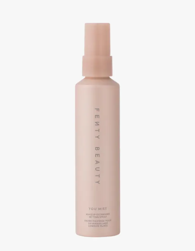 Fenty Beauty markasının, makyajın kalıcılığını artırma ve taze bir görünüm sağlama amacıyla tasarlanmış açık pembe You Mist makyaj sabitleyici sprey şişesi, sade bir beyaz arka plan üzerinde şık bir şekilde sergileniyor.