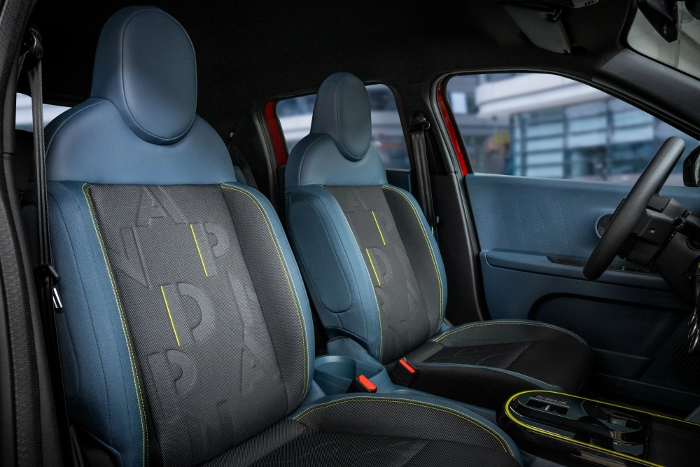 Fiat Grande Panda elektrikli SUV modelinin iç mekanında, modern mavi ve koyu gri kumaşla kaplı, sırtlarında kabartma PANDA yazıları ve belirgin sarı dikiş detayları bulunan özgün koltuklar görülüyor.