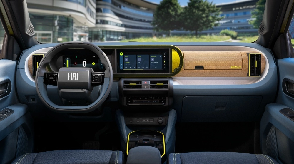 Fiat Grande Panda elektrikli SUV modelinin modern iç mekanında, dijital gösterge paneli ve üzerinde Fiat logosu bulunan direksiyon simidi, merkezi dokunmatik ekran, sarı vurgulu havalandırma ızgaraları ve Bambox yazılı ahşap görünümlü ön konsol detaylarıyla öne çıkıyor.