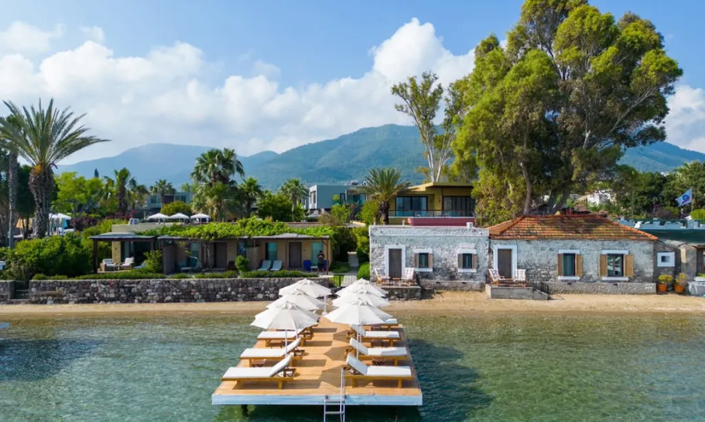 Flamm Bodrum Gölköy’de kum plaj, ahşap iskele, beyaz şemsiyeler ve berrak deniz manzarası