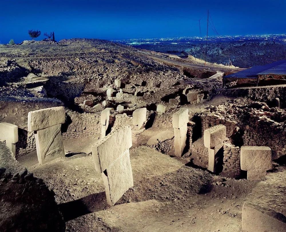 Şanlıurfa’daki Göbeklitepe arkeolojik alanının gece aydınlatmasında, erken Neolitik döneme ait T-şekilli anıtsal dikilitaşlar ve dairesel yapılar belirginleşirken, uzakta bir şehrin ışıkları Türkiye’deki 22 UNESCO Dünya Mirası rotasına eklenmeyi bekleyen bu kadim yeri aydınlatıyor.