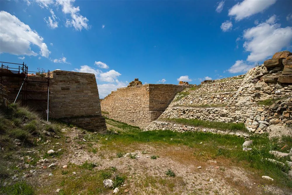 Türkiye'nin 2023'te UNESCO Dünya Mirası Listesi'ne giren Gordion Antik Kenti'nde, Kral Midas'ın efsanelerinin doğduğu topraklardaki Frig dönemine ait devasa taş surlar ve eğimli arazide yükselen sağlam savunma yapıları, bazı kısımlarında restorasyon iskelesiyle mavi gökyüzünün altında uzanıyor.