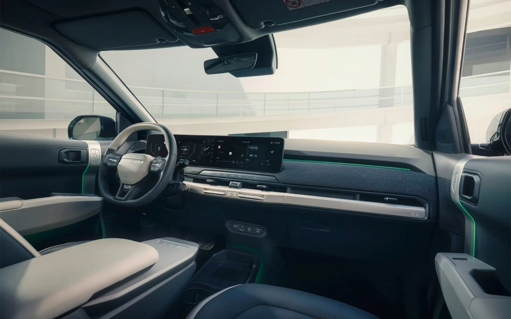 Kia EV3 SUV elektrikli otomobilin iç mekan tasarımını geniş açılı olarak gösteren bu görselde, sürücü koltuğundan bakıldığında modern direksiyon, geniş dijital gösterge paneli ve bilgi-eğlence ekranı, yeşil ambiyans aydınlatmalı fütüristik ön konsol ve ergonomik orta konsol detayları belirginleşiyor.