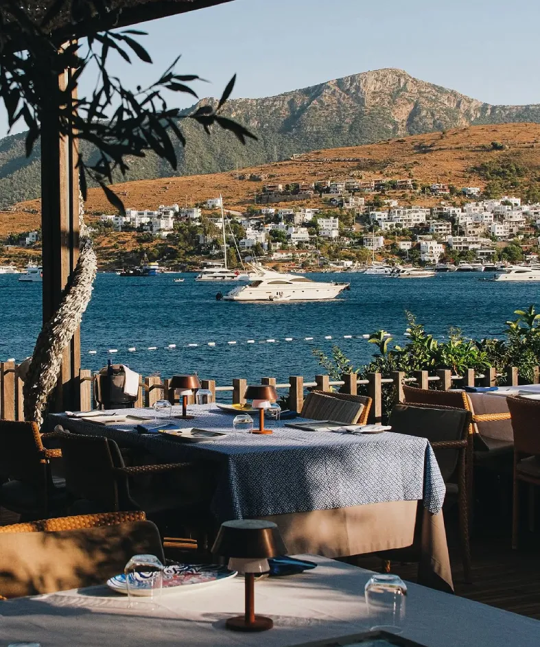 Maçakızı Beach Club Türkbükü’nde deniz manzaralı restoran, iskele alanı ve Bodrum koy manzarası
