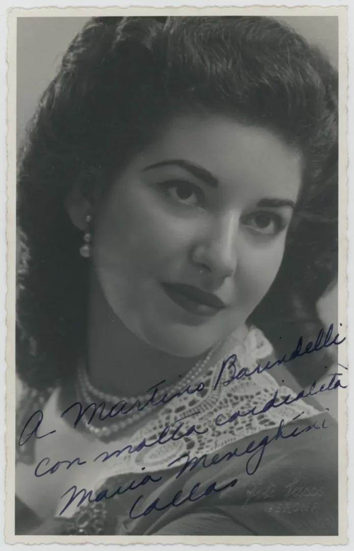 Siyah beyaz çekilmiş bu portre fotoğrafında, inci kolye ve küpeleri, belirgin dalgalı saçları ve dantel işlemeli yakasıyla zarafetini sergileyen dünyaca ünlü opera sanatçısı Maria Callas, doğrudan izleyiciye bakarak hafifçe gülümsüyor ve fotoğrafın üzerine kendi imzasını atmış.