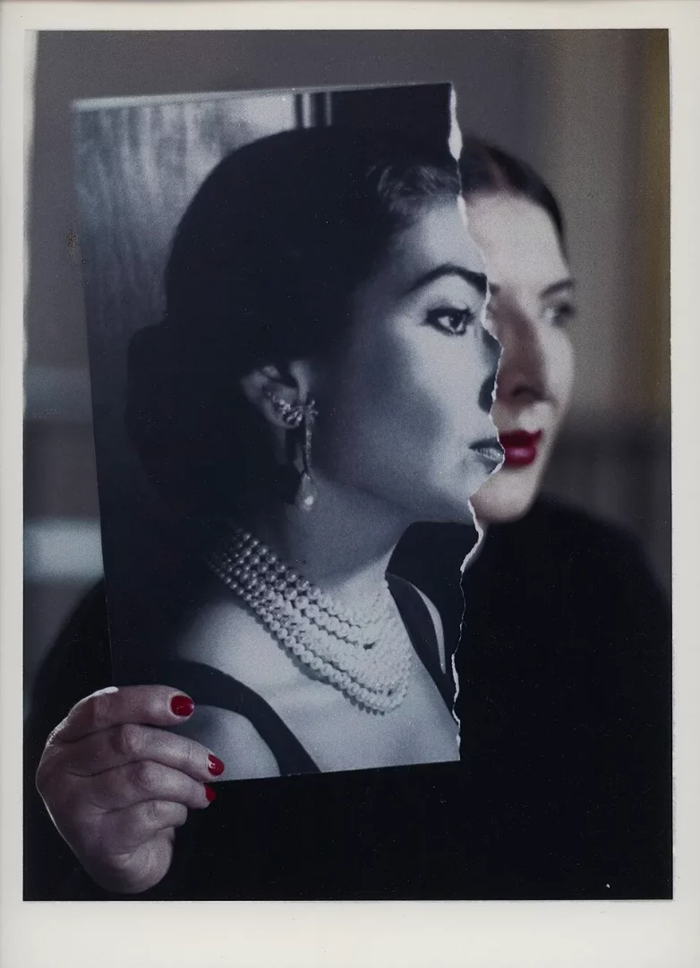 Kırmızı ojeli bir elin tuttuğu yırtık bir fotoğrafta, incili kolye ve gösterişli küpelerle yandan poz veren siyah beyaz Maria Callas portresi, arkadaki kırmızı rujlu kadınla birlikte sanatçının yaşamındaki karmaşık ve çok yönlü anları vurguluyor.