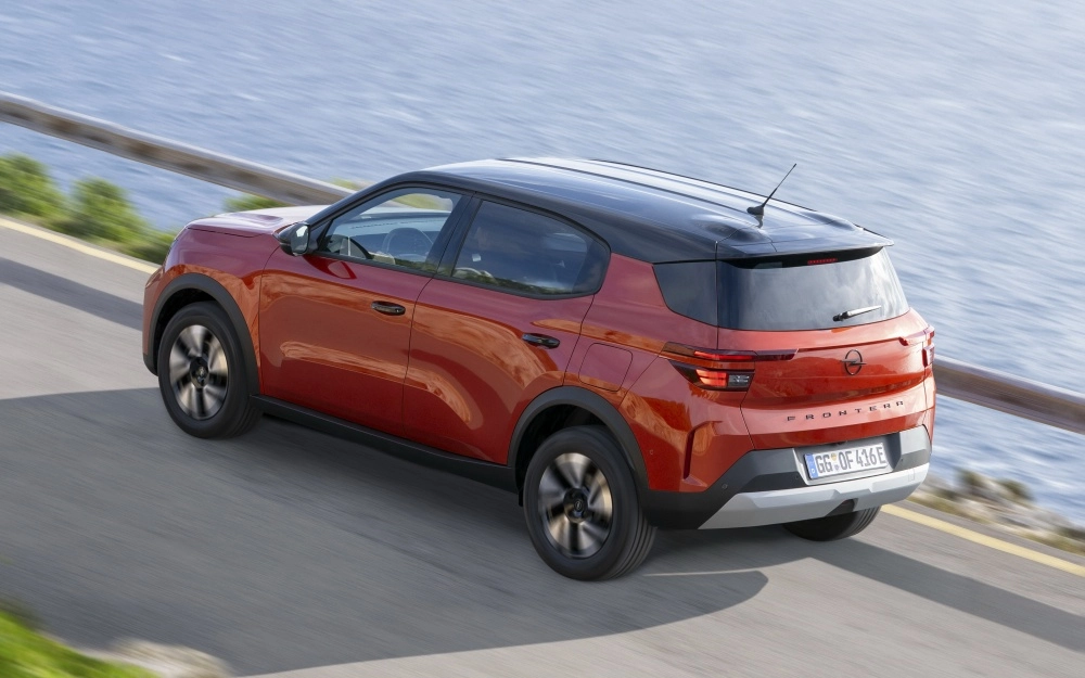Mavi denizin kenarındaki kıvrımlı yolda hızla ilerleyen, canlı kırmızı rengi ve siyah tavanıyla modern bir görünüm sunan Opel Frontera Electric'in dinamik açıyla çekilmiş etkileyici arka ve dış mekan tasarımı.