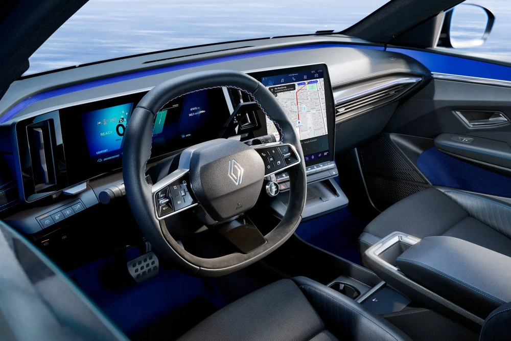 Renault Megane E-Tech elektrikli kompakt otomobilin modern iç mekan tasarımı, parlak mavi ambiyans aydınlatmasıyla vurgulanan gösterge paneli ve harita gösteren dikey dokunmatik multimedya ekranıyla fütüristik bir görünüm sunuyor; koltuklar ve kapı içlerindeki mavi dikişler bu şık iç mekanın tasarım detaylarını tamamlıyor.