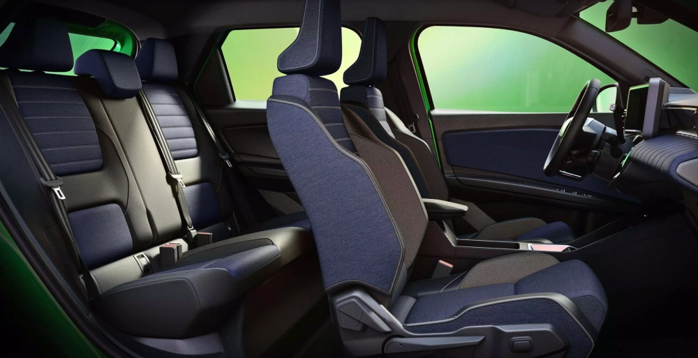 Renault R5 E-Tech modelinin, koyu mavi kumaş döşemeli ve siyah detaylarla bezeli, direksiyonu ve ön paneli de kısmen görünen modern iç mekan tasarımı, ferah bir atmosfer sunarak yolcu ve arka koltuklardaki rahatlığı vurguluyor.