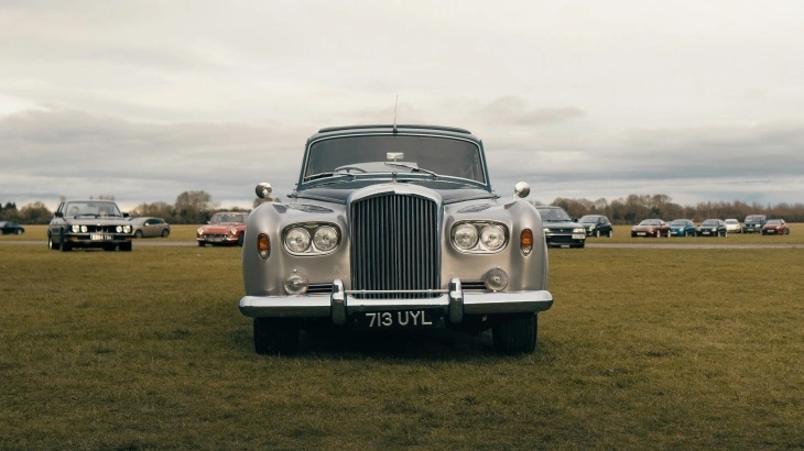 Rolls-Royce Silver Cloud, ön cepheden görünümüyle geniş ızgarası ve zarif tasarımıyla dikkat çekiyor. Arkada farklı klasik otomobillerin de yer aldığı açık alanda sergileniyor.