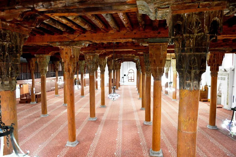 Türkiye'deki UNESCO Dünya Mirası listesinde yer alan Sivrihisar Ulu Camii'nin, Selçuklu zanaatkârlığının nadide örneklerinden ahşap sütunları ve kündekâri tekniğiyle bezenmiş tavan kirişlerini gösteren iç mekân görüntüsü.