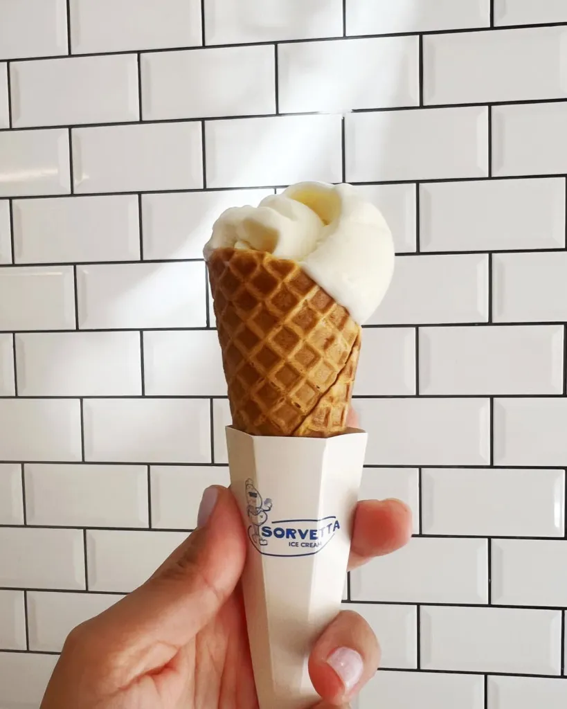 Beyaz metro fayansları önünde, açık renk ojeli bir el, üzerinde Sorvetta logosu bulunan özel karton tutacaklı, hafifçe eriyerek waffle külahından taşan bol ve kremsi vanilyalı dondurmayı serinletici bir lezzet olarak sunuyor.