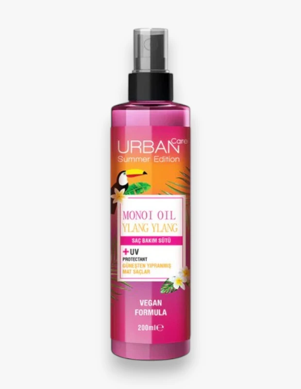 Pembe spreyli Urban Care Monoi Oil Ylang Ylang Saç Bakım Sütü şişesi, turuncu ve pembe etiketinde toucan kuşu, palmiye yaprakları ve beyaz çiçekler ile yaz temalı tasarımıyla güneşten yıpranmış mat saçlara özel UV koruyuculu vegan formülünü vurguluyor.