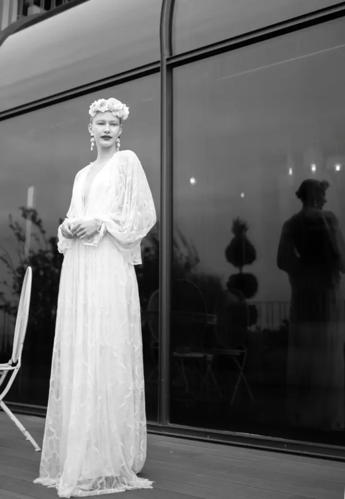 Uzun kollu, transparan dantel detaylı bohem gelinlik. Çiçek tacı ve vintage ilhamlı siluetiyle romantik ve sanatsal bridal görünüm sunan tasarım.