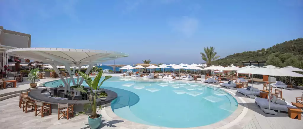 Bodrum'da, Ege Denizi manzaralı lüks bir otelin geniş yüzme havuzu, ortasında kendine özgü beyaz bir gölgelikle çevrili şık bir havuz barı ve etrafında beyaz şezlonglar, şemsiyeler ile yeşil tepelerin çevrelediği, davetkar bir dinlenme alanı sunuyor.