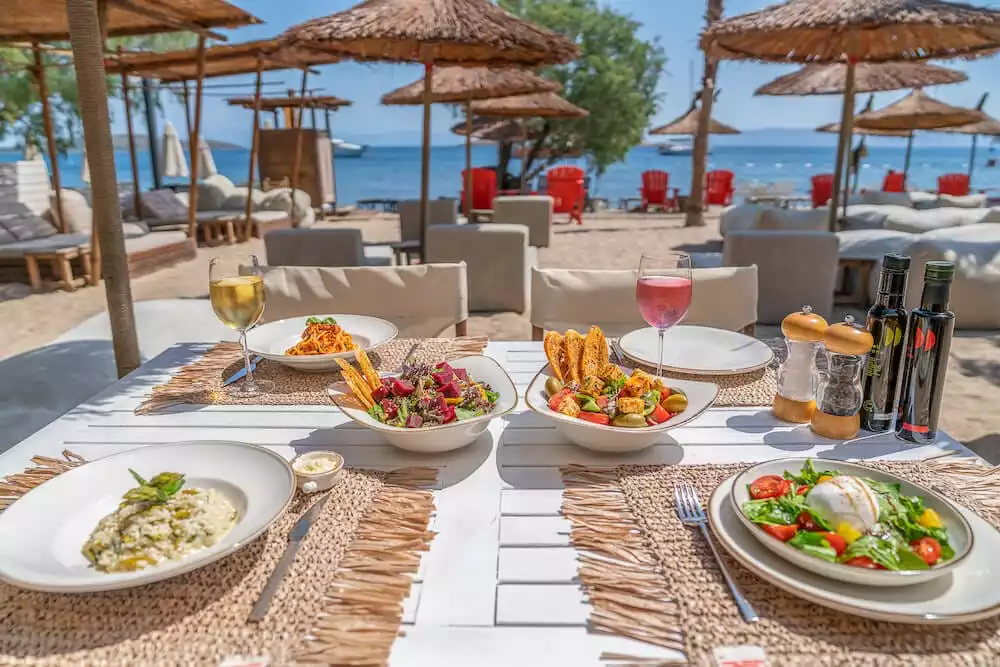 Bodrum'da, masmavi denizin kıyısında, hasır şemsiyelerin gölgelediği beyaz bir masada; özenle hazırlanmış bol çeşitli makarnalar, taze salatalar, kadehlerde şaraplar ve yemek için gerekli zeytinyağları ile süslenmiş, güneşli ve davetkar bir yemek ortamı.