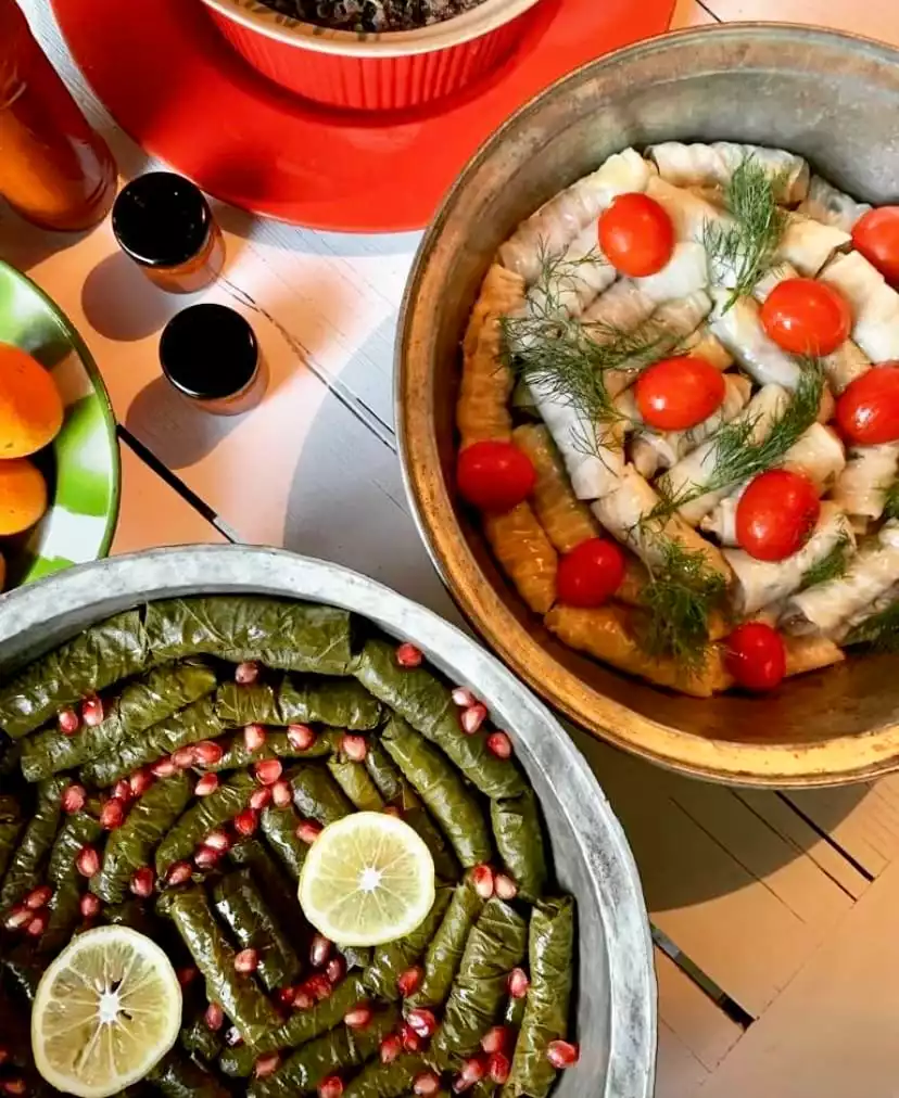 Yakın çekimdeki bu karede, nar taneleri ve limon dilimleri ile süslenmiş taze yaprak sarmalar ile cherry domatesler ve dereotu eşliğinde servis edilen lahana sarmalarının bulunduğu iki büyük metal tepsi, geleneksel Türk mutfağının zenginliğini sunuyor.