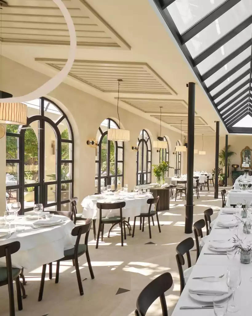 Bodrum'da bulunan bu şık ve aydınlık restoranda, kemerli pencerelerden giren doğal ışıkla aydınlanan beyaz örtülü masalar ve koyu renk sandalyeler modern bir ambiyans sunarken, yüksek tavan ve cam ışıklık ferah bir yemek deneyimi vaat ediyor.