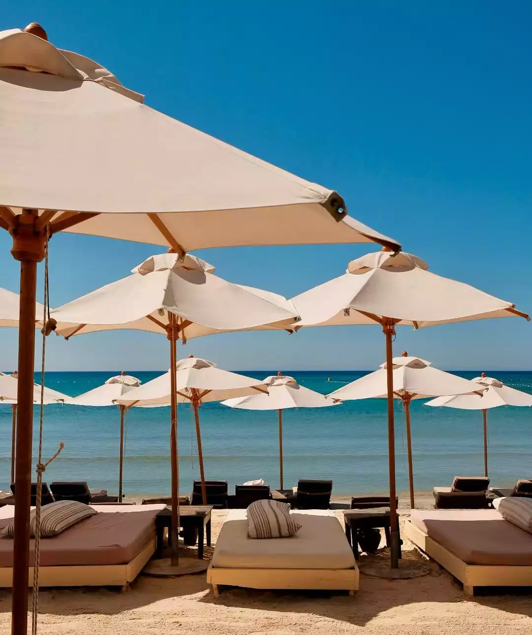 Geniş beyaz şemsiyeler ve altında konumlanmış rahat şezlonglarla dolu Fly-Inn Beach'in sıcak kumlu sahilinde, berrak turkuaz denizin ve masmavi gökyüzünün eşlik ettiği huzurlu bir dinlenme ortamı sunuluyor.