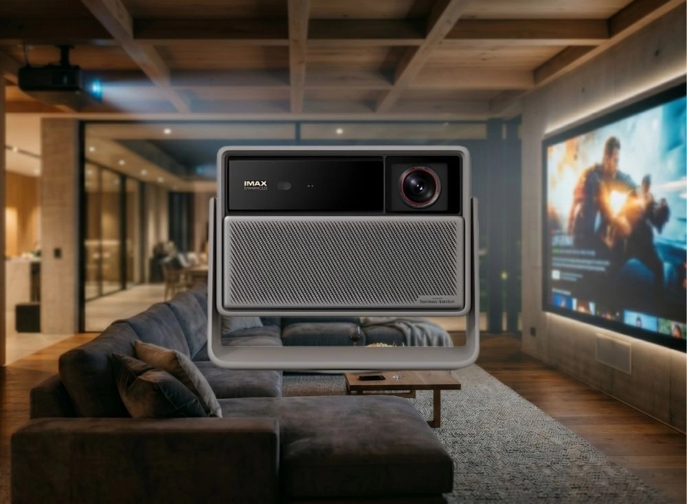 Büyük bir ekranda aksiyon filmi yansıtılan, ahşap tavanlı modern bir ev sineması odasında konumlanmış, üzerinde IMAX Enhanced ve Harman Kardon yazıları bulunan, gri-siyah premium bir projeksiyon cihazı, sofistike bir eğlence ortamını sergiliyor.