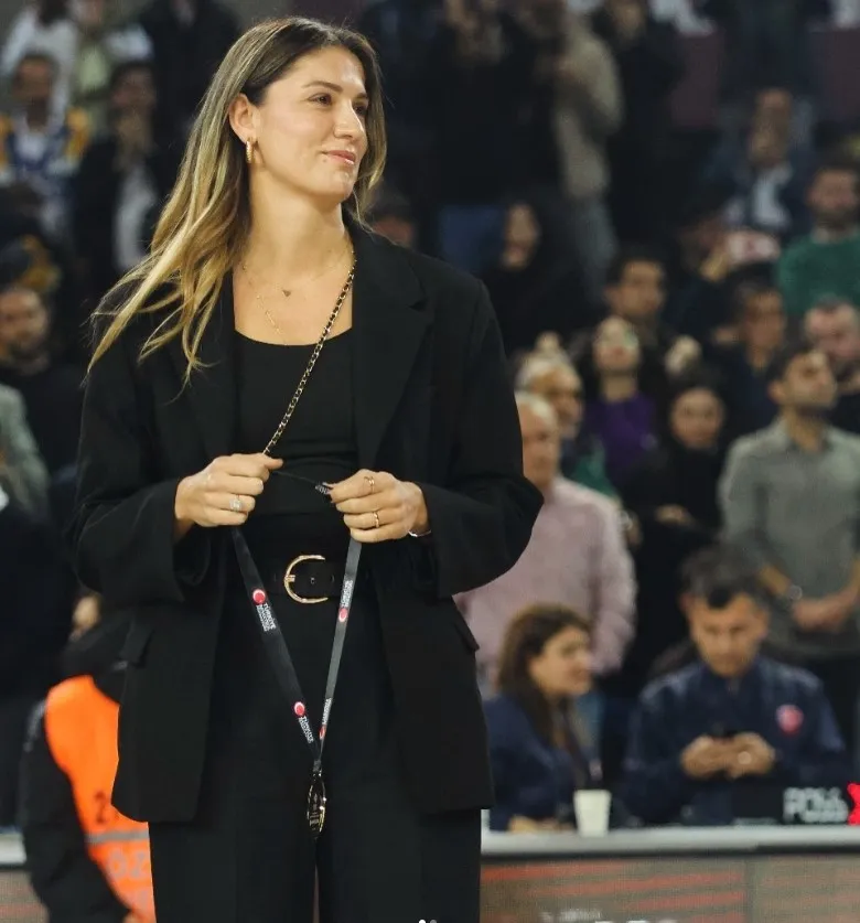 Türk milli basketbolcu Bahar Çağlar Ökten, siyah takım elbisesiyle bir basketbol maçında saha kenarında görüntüleniyor.