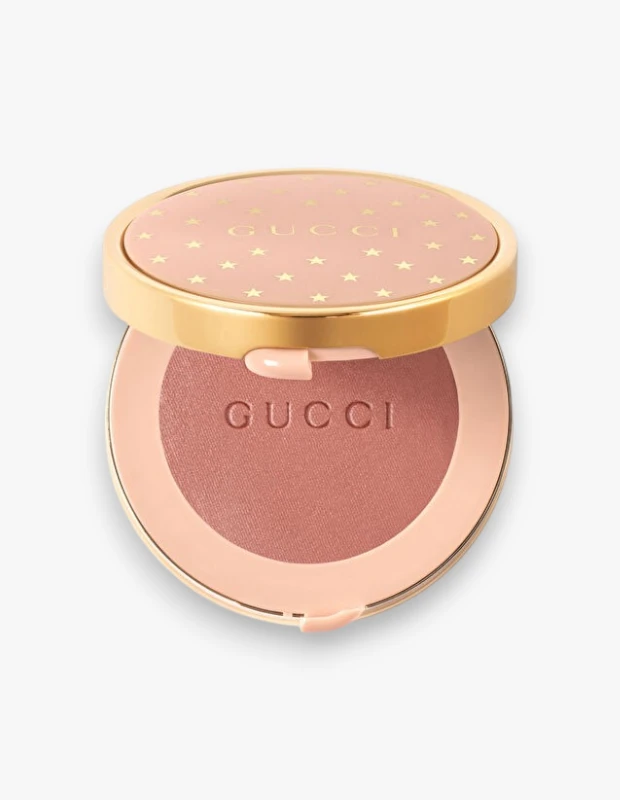 Gucci Beauty markasına ait 05 Rosy Beige rengindeki allık, altın çerçeveli ve üzerinde altın rengi yıldız desenleri ile Gucci yazısı bulunan pembe kapağı açık şekilde, kutunun içindeki gül beji tonunu ve kabartmalı Gucci logosunu sergiliyor.