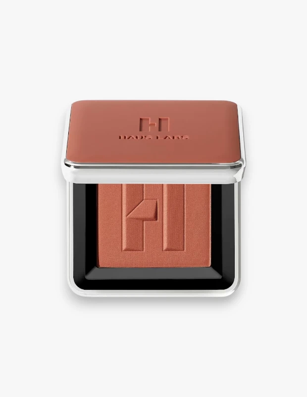 Yarı açık kapağıyla beyaz zeminde duran, metalik gümüş kenarlıklı ve turuncu-kahve tonlarındaki Haus Labs Color Fuse Blush Fire Moon allık paleti, hem kapağında hem de allığın yüzeyinde markanın kabartmalı H logosunu sergiliyor.