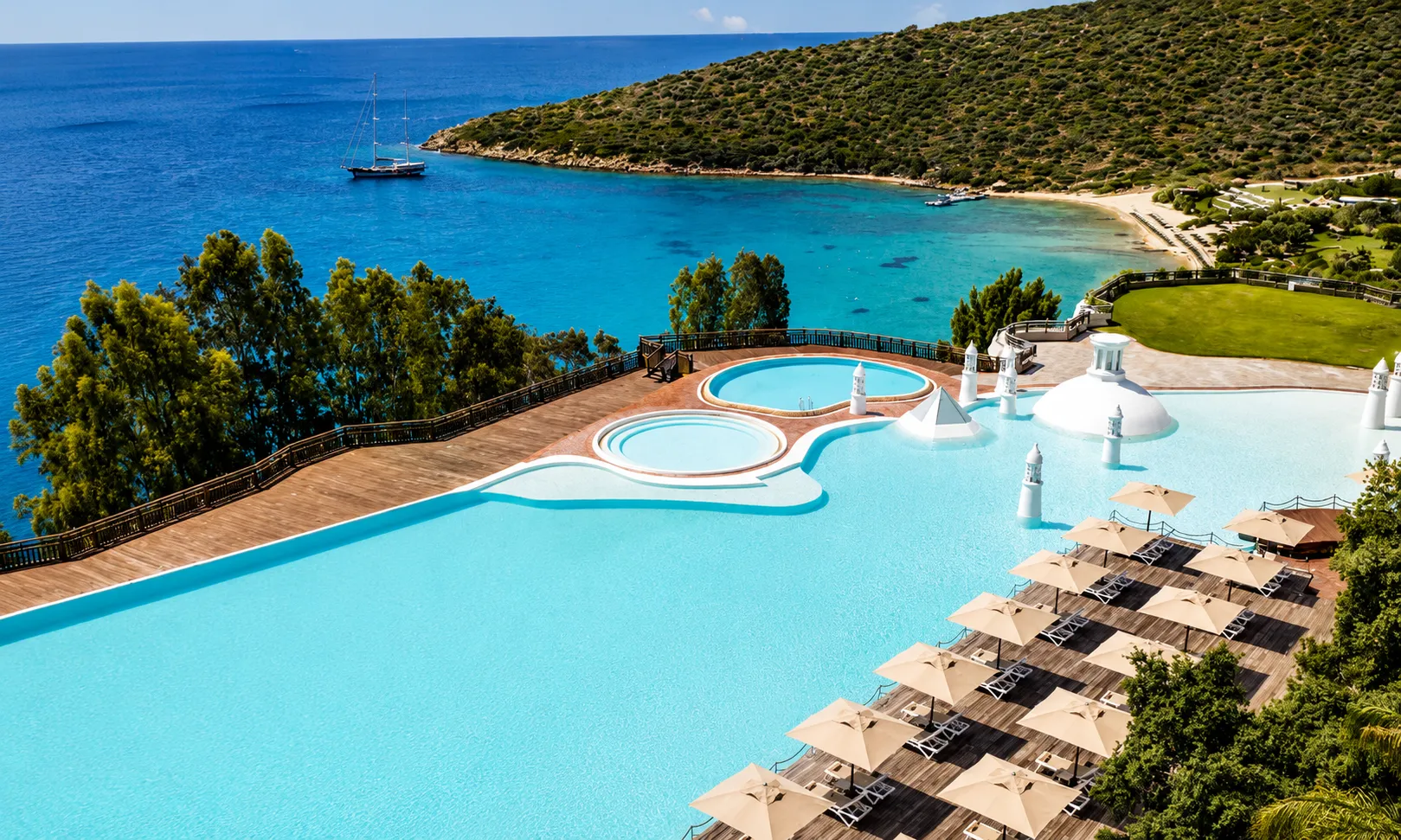 Kempinski Hotel Barbaros Bay Yalıçiftlik’te turkuaz koy, ahşap güneşlenme terasları, lüks plaj alanı ve deniz manzarası