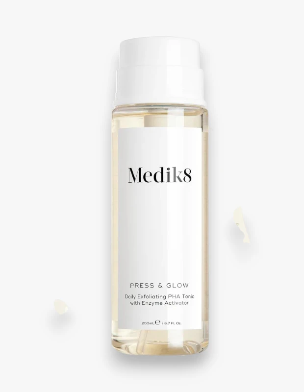 Beyaz kapaklı ve şeffaf şişesinde, Medik8 Press & Glow Daily Exfoliating PHA Tonic with Enzyme Activator etiketi bulunan, 200 ml'lik bu cilt toniği, cilde ışıltı veren ve nazikçe peeling yapan bir formüle sahip olup çevresinde birkaç damlası görülmektedir.