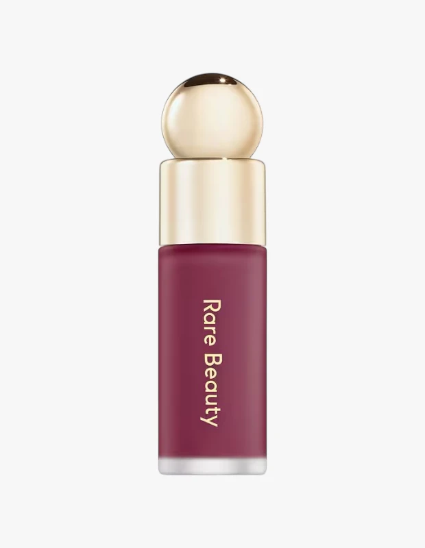 Sonbaharda trend olan allık tonları arasında öne çıkan Berry Sorbet görünümünü yansıtan Rare Beauty Soft Pinch Liquid Blush Faith tonu, koyu mürdüm rengi formülü, zarif altın renkli küresel kapağı ve şişe üzerindeki altın renkli marka detayıyla sade beyaz bir zeminde sergileniyor.