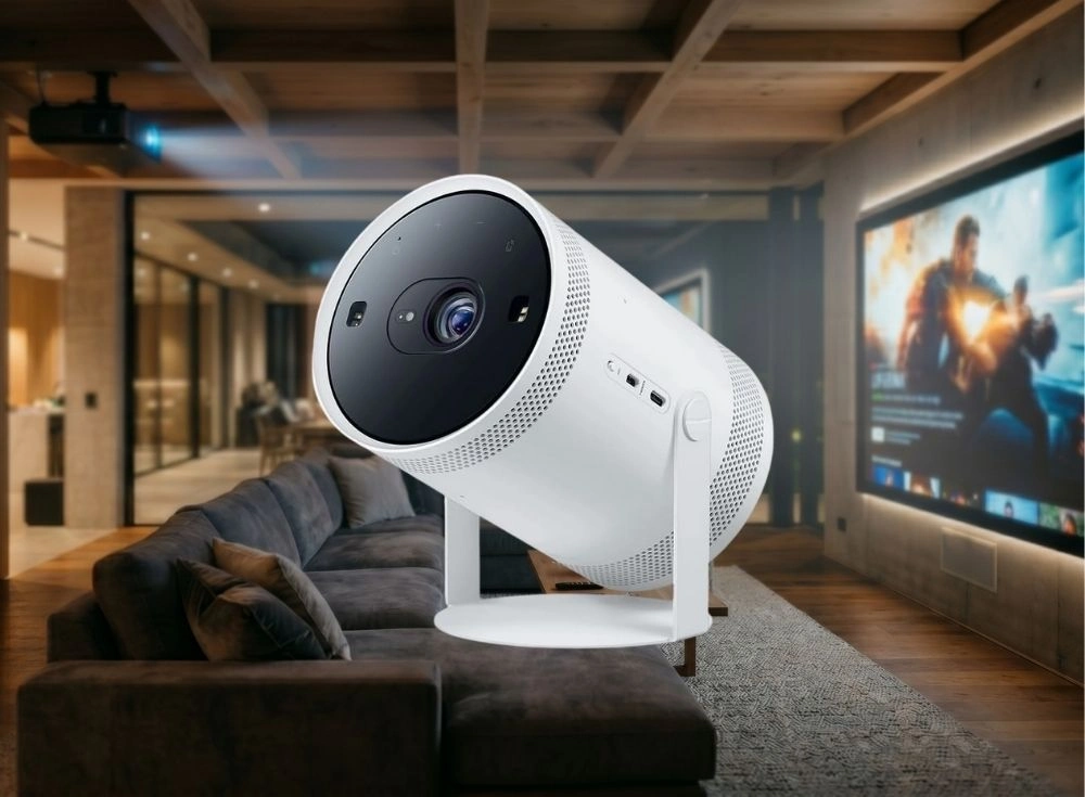 Modern bir oturma odasında, siyah lensi ve ızgaralı yüzeyi olan beyaz renkli Samsung The Freestyle 2 taşınabilir akıllı projeksiyon cihazı, büyük bir ekrana Full HD görüntü yansıtırken konumlandırılmış.