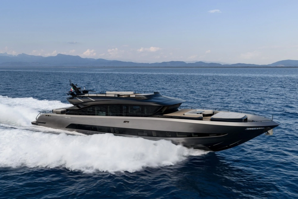 Güneşli bir denizde zarifçe süzülen, modern ve aerodinamik tasarımlı, lüks detaylarıyla dikkat çeken AB Yachts 110 süper yat, beyaz gövdesi ve geniş pencereleriyle Akdeniz'in turkuaz sularında ileri doğru hareket ediyor.