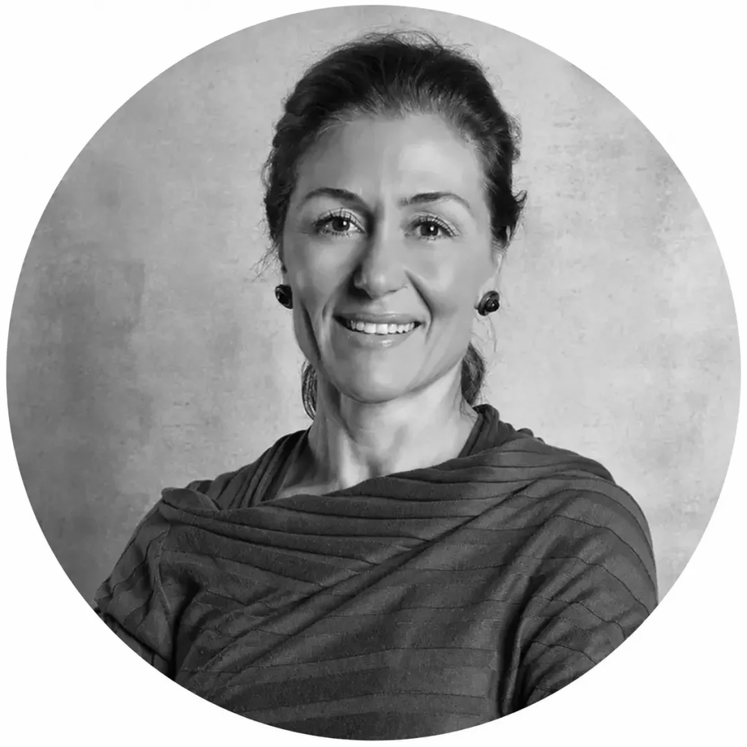 Feride Çelik'in koyu renk, dokulu bir üst giydiği, saçları toplanmış ve küçük küpeleriyle kadraja giren, yüzünde samimi bir gülümsemeyle doğrudan objektife baktığı siyah beyaz, dairesel bir portre fotoğrafı.
