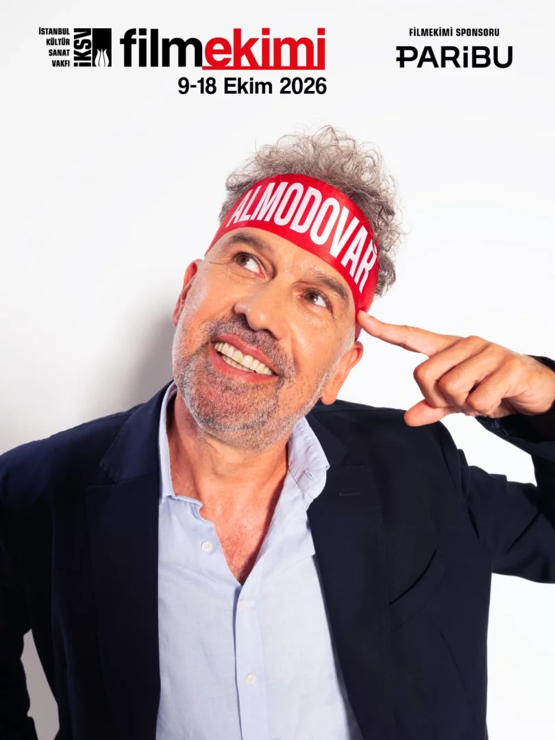 Filmekimi afişinde, gri kıvırcık saçlı, sakallı, kırmızı ALMODOVAR yazılı saç bandı takmış bir adam, lacivert ceketinin ve açık mavi gömleğinin içinde neşeyle gülümsüyor ve işaret parmağıyla şakağını göstererek yukarı bakıyor.