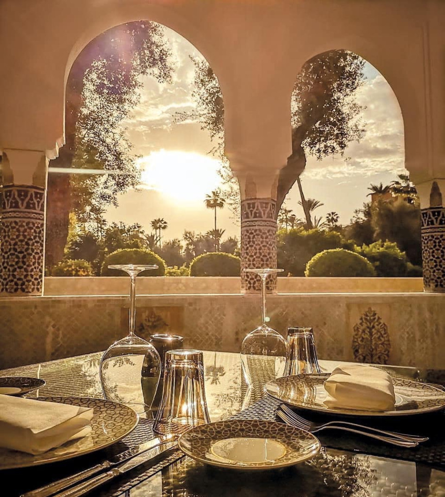 Marakeş'in ünlü Le Marocain restoranında, günbatımının altın rengiyle parlayan yemyeşil bahçeye bakan iki zarif kemerli pencereden, şık Fas seramikleri, parlayan kadehler ve beyaz peçetelerle hazırlanmış, davetkar bir yemek masası görülüyor.