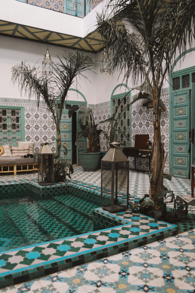 Marakeş'in eşsiz atmosferini yansıtan bir riad avlusunda, turkuaz ve geometrik desenli zellige karolarıyla bezenmiş serin havuzun etrafında yükselen hurma ağaçları ve zarif fenerler, Fas mimarisinin renklerle uyanan rüya gibi dokusunu gözler önüne seriyor.