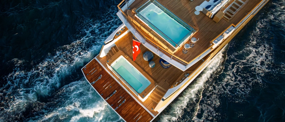 Güneşli bir denizde süzülen, modern ve şık hatlara sahip Numarine 40MXP explorer süper yatın geniş güverteleri ve panoramik pencereleri lüks yolculuk deneyimini vurgularken, yatın genel tasarımı denizde keşif için ideal bir profil sergiliyor.