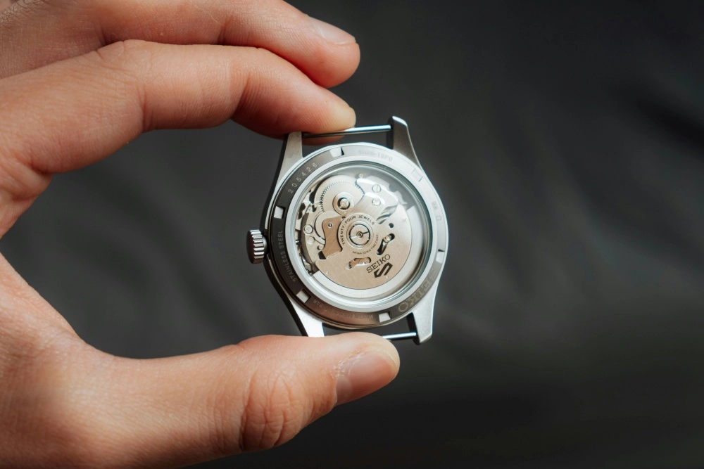 Yakın çekim bir görselde, bir elin tuttuğu Seiko 5 otomatik saatin şeffaf arka kapağından, mekanik aksamın hassas çarkları ve otomatik kurma görevini üstlenen SEIKO 5 logolu rotor net bir şekilde görülmektedir.