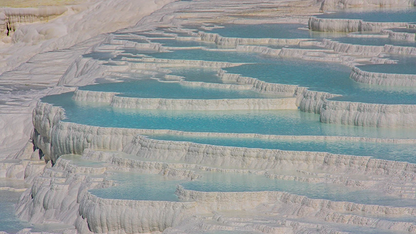 Denizli'deki Pamukkale'nin meşhur doğal oluşumu, kademeli beyaz traverten teraslarının berrak, mineral bakımından zengin turkuaz sularla dolup taştığı büyüleyici ve ikonik bir manzarayı gözler önüne seriyor.