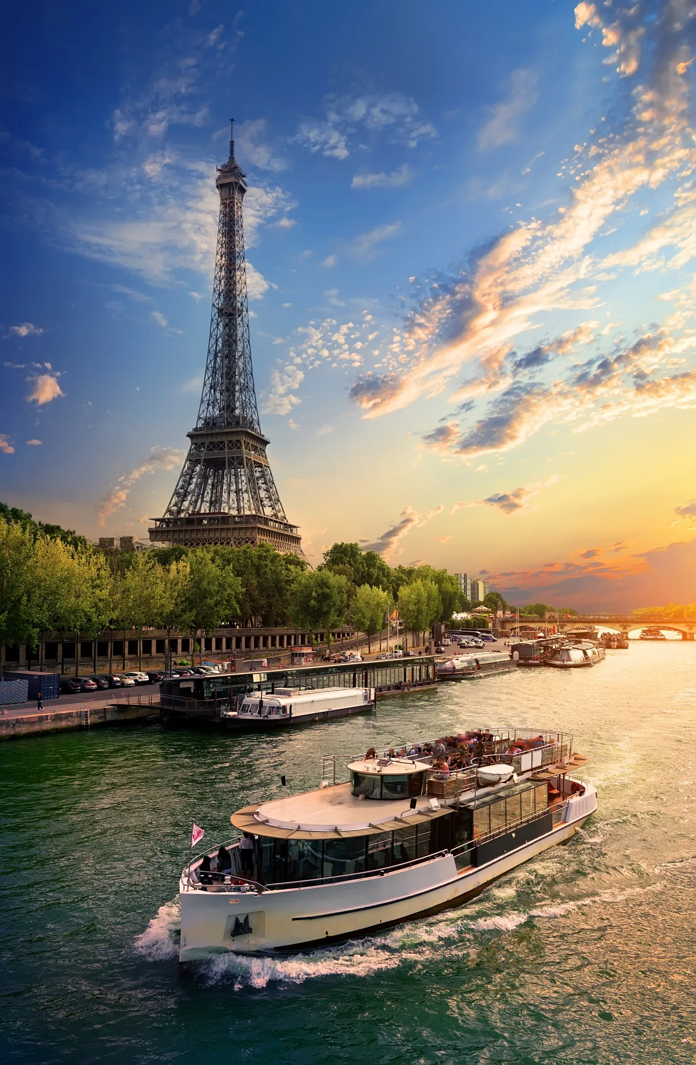 Eyfel Kulesi'nin yükseldiği, Sen Nehri'nde bir yolcu teknesinin süzüldüğü ve gün batımı renklerinin gökyüzünü süslediği bu büyüleyici Paris manzarası, yeni evli çiftler için unutulmaz bir balayı deneyiminin başlangıcını simgeliyor.