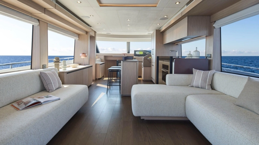 Prestige F6.7 flybridge yatın geniş ve aydınlık iç mekanında, lacivert okyanusa bakan büyük pencereler, açık renk konforlu koltuk takımları, entegre modern mutfak alanı ve gemi kaptan köşkü bir arada görülüyor, denizle iç içe lüks bir yaşam alanı sunuyor.