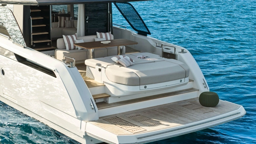 Masmavi denizde süzülen beyaz bir Prestige flybridge yatın kıç güvertesinde, çizgili yastıklarla zenginleştirilmiş geniş bir güneşlenme alanı, ahşap masalı rahat bir oturma grubu ve teak zeminli yüzme platformu lüks ve konforlu bir dinlenme alanı sunmaktadır.
