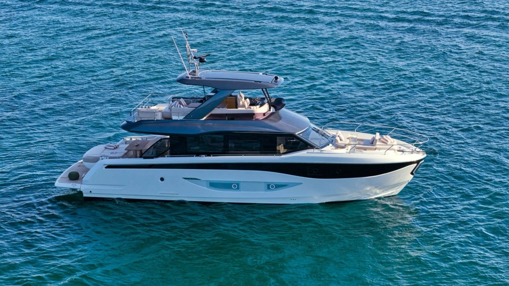Mas mavi dalgalı sularda zarifçe süzülen, beyaz gövdeli ve koyu gri üst yapı detaylarına sahip, lüks Prestige flybridge yat, ferah üst güvertesinde konforlu oturma alanları ve kaptan köşkü ile çağdaş bir deniz yaşamını sergiliyor.